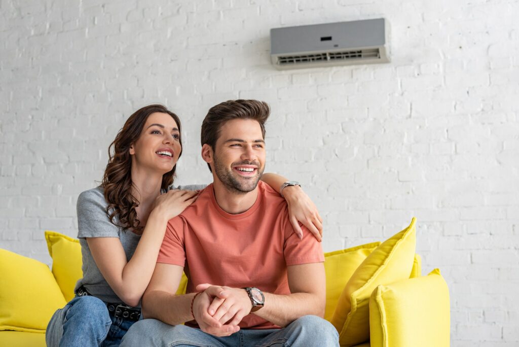 happy couple sitting on yellow sofa under air conditioner at home