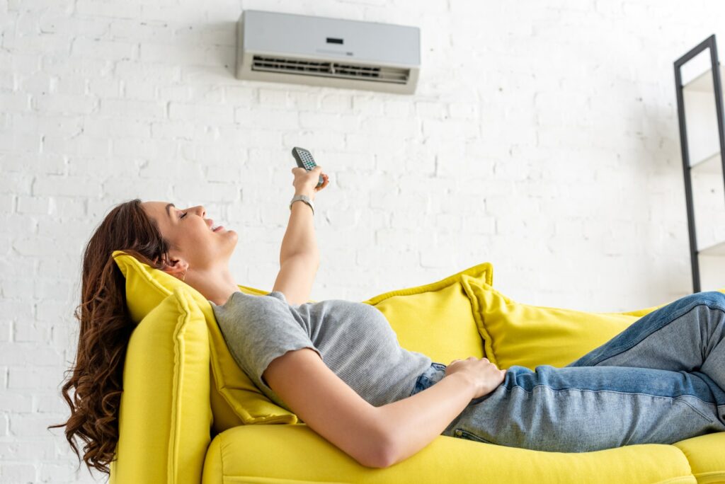 attractive young woman relaxing under air conditioner and holding remote control