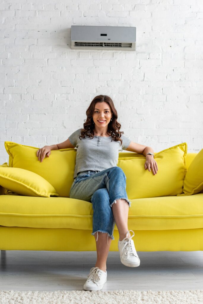 beautiful smiling woman sitting on yellow sofa under air conditioner at home