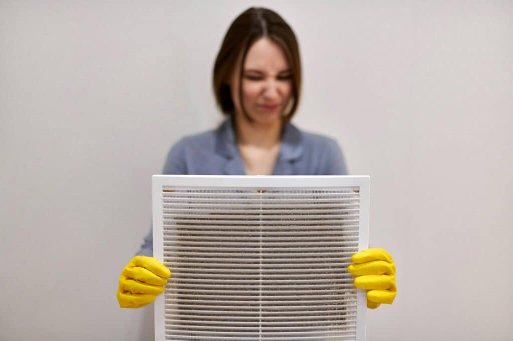 Woman holding dirty clogged AC filters, indicating poor maintenance.